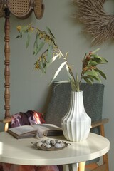 A vase of mimosa branches, an open book, a brass plate of eggs on a round table. A retro-style...