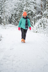 Fototapeta na wymiar A beautiful young woman in a winter wonderland enjoying the snow fashion walk wearing colourful jacket and hat