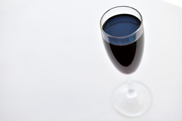 Small glass of red wine on a white background with shadows