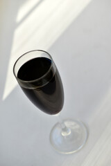 Small glass of red wine on a white background with shadows