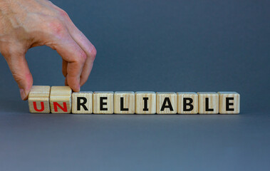 Unreliable or reliable symbol. Businessman turns wooden cubes and changes the word unreliable to reliable. Beautiful grey background, copy space. Business and unreliable or reliable concept.