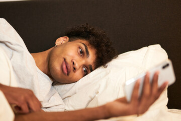 New message. Close up portrait of attractive brunette guy lying in the bed at home, resting and...
