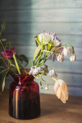 a beautiful fading bouquet of spring blooms and tender delicate tulips in a vase on a blue wooden background - 423442188