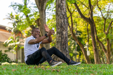 Portrait of a happy African American man using a cellular mobile phone in the garden park. Concept of 5G wireless technology, High-speed Internet, Global network telecommunication, Smart communication