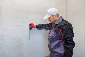 A man, an electrician marks out holes for sockets with a pencil, a tape measure