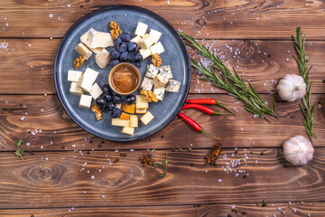 A plate with sliced cheese, honey, grapes on a wooden background, decorated with spices, rosemary, garlic.