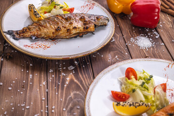 Grilled fish on a plate with vegetables, bell pepper, coarse salt on a brown wooden background.