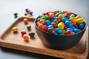 Bright candy drops in a black bowl on a wooden tray. Festive mood.