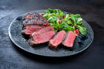 Modern style traditional dry aged sliced wagyu roast beef with corn salad and pine nuts served as close-up on a Nordic design plate