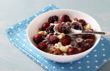 Granola crispy with natural yogurt, frozen cherry and blackberry, chocolate and nuts in white bowl on blue background. Close-up