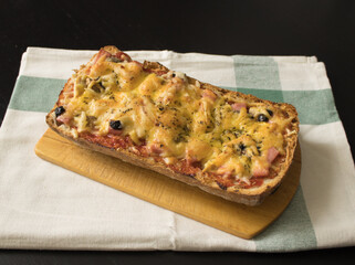 Homemade freshly prepared bruschetta / pizza with sausage, tomatoes, olives, cheese and seasonings on an old wooden board on a cotton towel. Simple and delicious food 