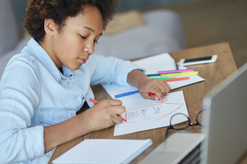 Naklejka premium Portrait of focused teen schoolgirl using markers while doing her homework with laptop computer at home