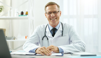 Joyful doctor sitting at the table with documents at work