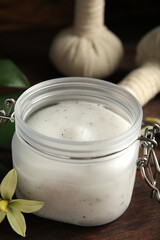 Jar of salt scrub and orchid flower on wooden table, closeup