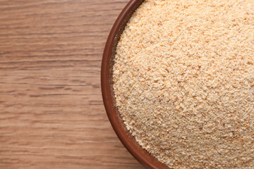 Fresh bread crumbs in bowl on wooden table, top view. Space for text