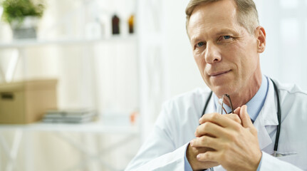 Good-looking male doctor holding glasses against blurred background