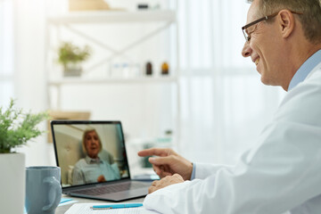 Fototapeta premium Cheerful doctor providing online consultation to old woman in clinic