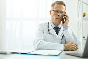 Serious doctor talking on mobile phone and using laptop at work