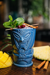 Refreshing cold Tiki Drink Cocktail with pineapple, mango, mint and cinnamon 