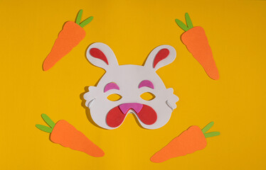 Cute bunny mask and colorful carrots on yellow and vivid background. Easter decoration