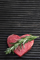 Heart shape raw fresh beef steak with rosemary stick on metal grill background