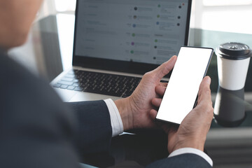 Mockup image, business man hand holding mobile smart phone working on laptop computer at office