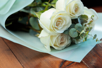 A bouquet of white roses in paper packaging lies on a wooden table.