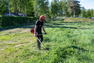 Right side view at teenage boy mowing grass with handheld gasoline lawn mower. He wears eye and ear protection headphones. Health and safety concept, worker job protection.Safe work conditions