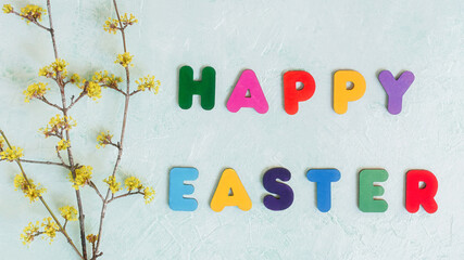 Happy Easter. Wooden multicolored letters and a blooming twig on a mint background. Greeting card, horizontal banner, copy space, top. Creative Easter composition in bright colors, flat lay. Handmade