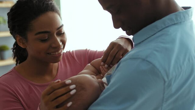 Happy parenthood. African american mother and father giving water to newborn baby from kid bottle
