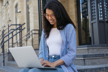 African American business woman using laptop computer, searching information, communication online. Smiling freelancer typing on laptop, working project outdoors. Successful business concept