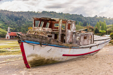 Fototapeta na wymiar Shipwreck at Chullec Bay Quinchao, Los Lagos, Chile with Santa Maria de la Candelabria Church in the background