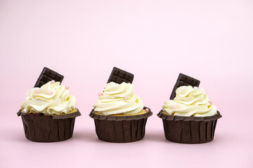  Set  cupcakes with vanilla cream decorated with  pink beads  and chocolate on pink background with  copy space for text .