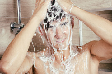 The athletic guy takes a shower. Body care and hygiene. Foam on the head.
