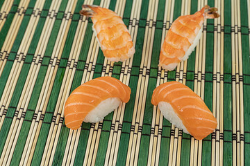 four sushi nigiri with salmon and shrimp on a bamboo mat close-up