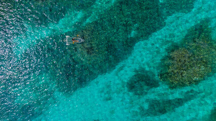 サンゴ礁が透けるケラマブルーの海にクリアカヤックで浮かぶドローン俯瞰写真