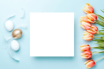 Easter background blue. Golden, white colour egg in basket with spring tulips, feathers on pastel blue background in Happy Easter decoration. Flat lay, top view.