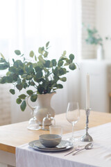 Elegant gray cup on a table in white kitchen and a vase with twig of eucalyptus. Spring pretty background. Morning romantic mood. Shabby chic style. Morning tea or coffee. Tender beautiful decor