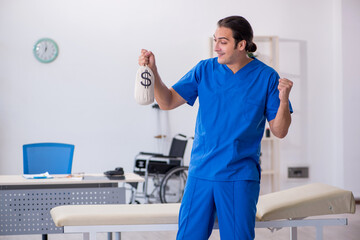 Young male doctor holding moneybag in the clinic