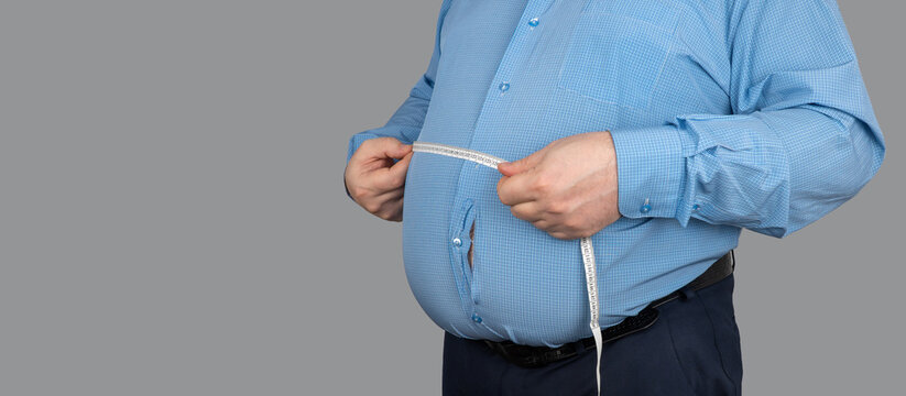 fat guy measures the size of the abdomen with a centimeter measuring tape. shirt was torn because of the large fat deposits. business man is obese and decided to stick to a diet. Losing Weight Day.