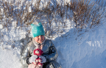 Fototapeta na wymiar In the forest in winter on a frosty sunny day, a girl sits on the snow and holds a plush toy in her hands.
