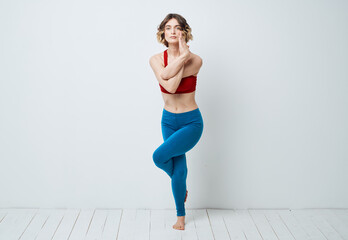 A woman in blue leggings does exercises on a light background of yoga asana
