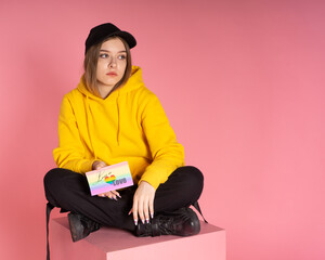 Girl sits on a pink cube and holds a card with the words love is love and lgbt heart