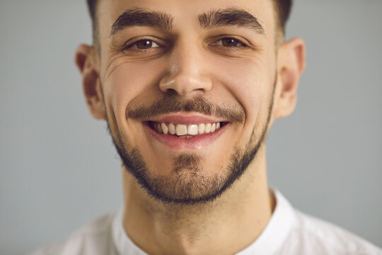 Closeup Studio Portrait Of Happy Cheerful Amiable Young Caucasian Man With Stubble, Friendly Candid Open Smile And Crow's Feet Wrinkles Around His Kind Eyes. Human Face, People's Appearance Concept