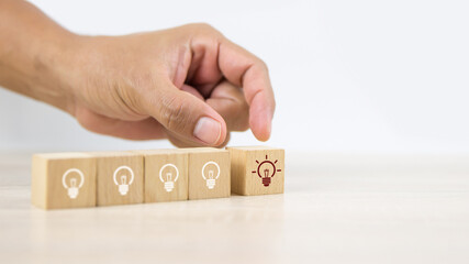 Close up hand choosing light bulb or lamp icons on cube wooden toy blocks concepts human resources for business leadership and creativity.