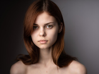 Red-haired woman with bared shoulders portrait close-up dark background model