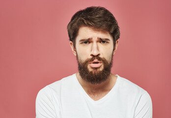 Portrait of an upset man in a white t-shirt on a pink background cropped view