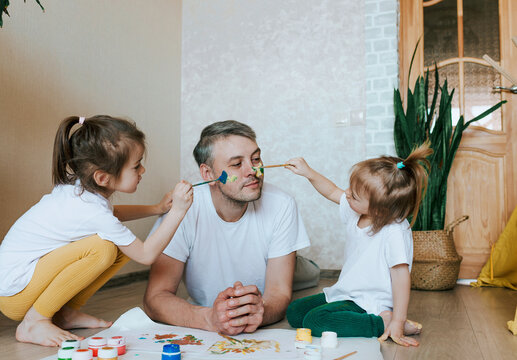 two little girls paint on dad's face with paint