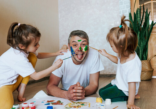 two little girls paint on dad's face with paint