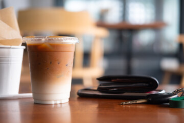 Iced coffee latte in plastic glass with men wallet and car key on wood table.